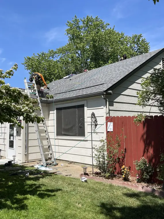 The Royal Roofing crew mid tear-off on a cream-sided house, a ladder against the eave