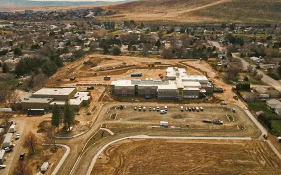 Wide aerial of a campus under construction with roof work under way in the distance