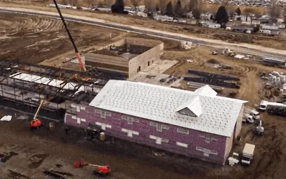 A crane lifting roofing materials onto a new building with underlayment already on