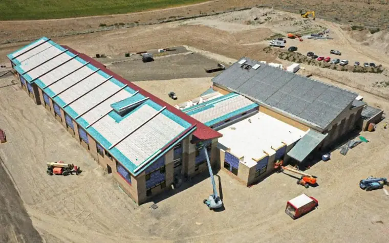 Aerial view of commercial membrane roofs with teal parapet trim and a lift on site