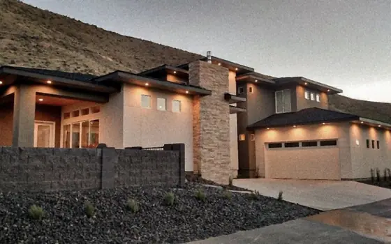 A modern stucco home at dusk under a bare hillside